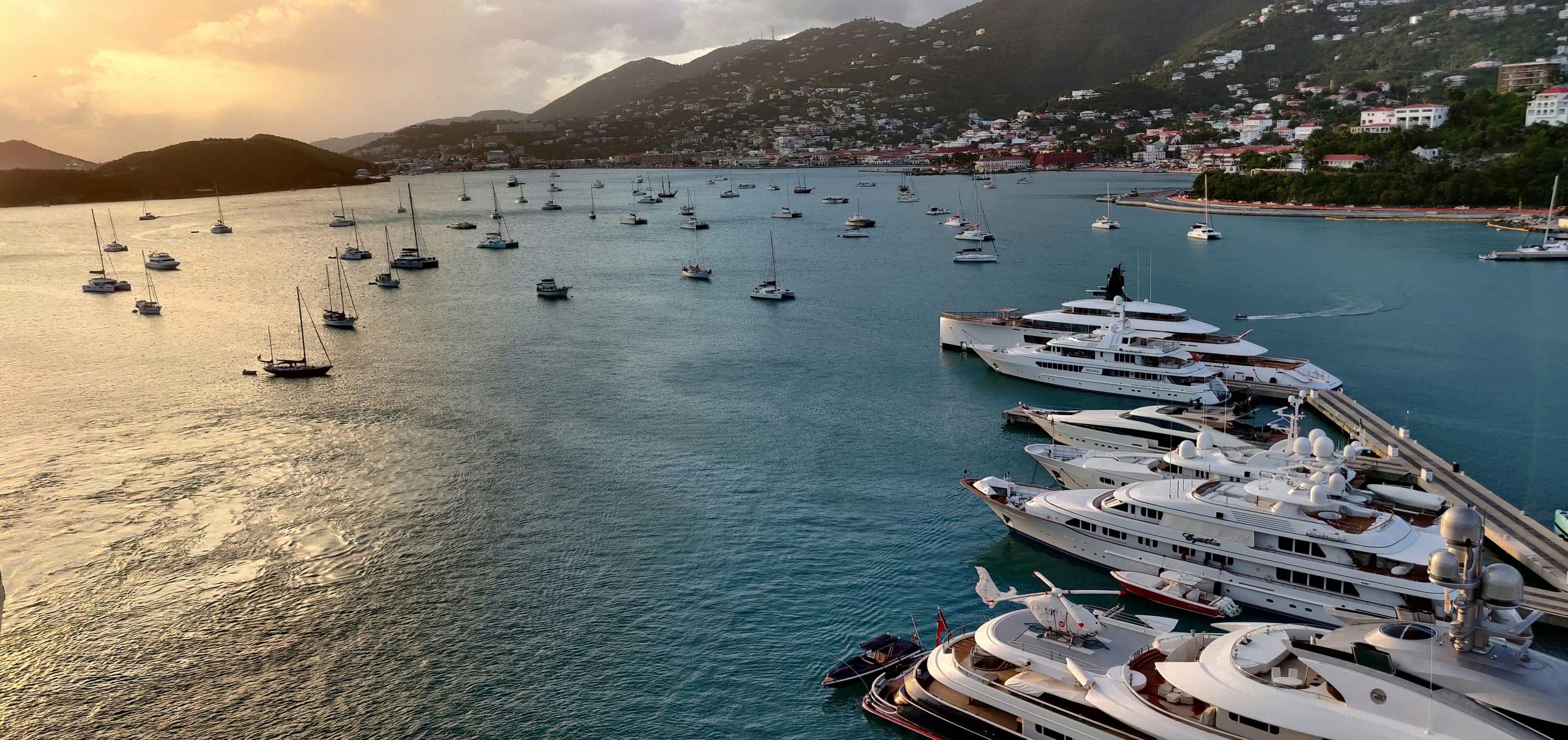 Superyachts moored at a marina in Charlotte Amalie harbour, St Thomas, at sunset, one with a helicopter on deck