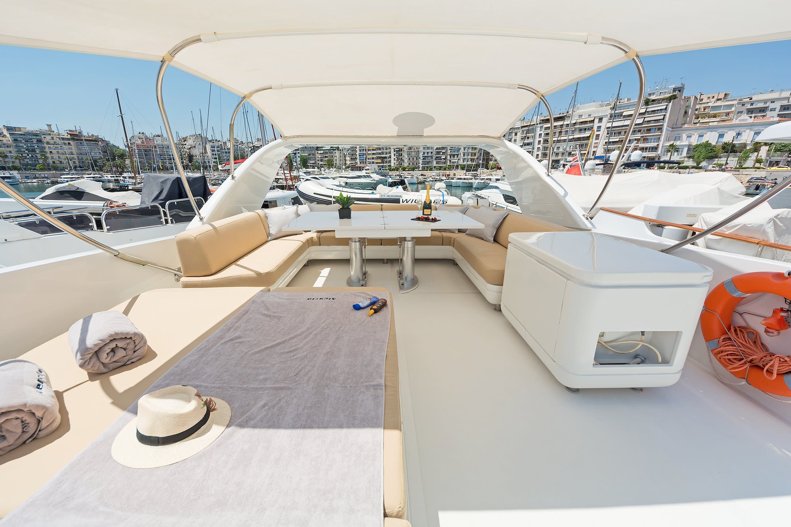 ALEGRIA - shaded deck seating with sun hat and towels, marina behind | Drivas Yachts