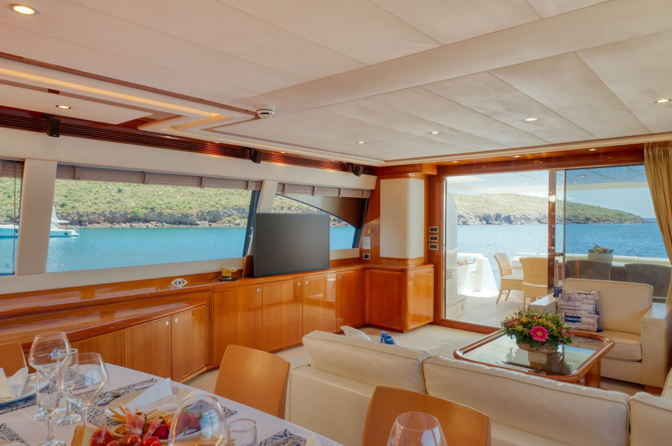 LIDIA - main saloon with cream sofas, TV, wood cabinetry and dining table | Drivas Yachts