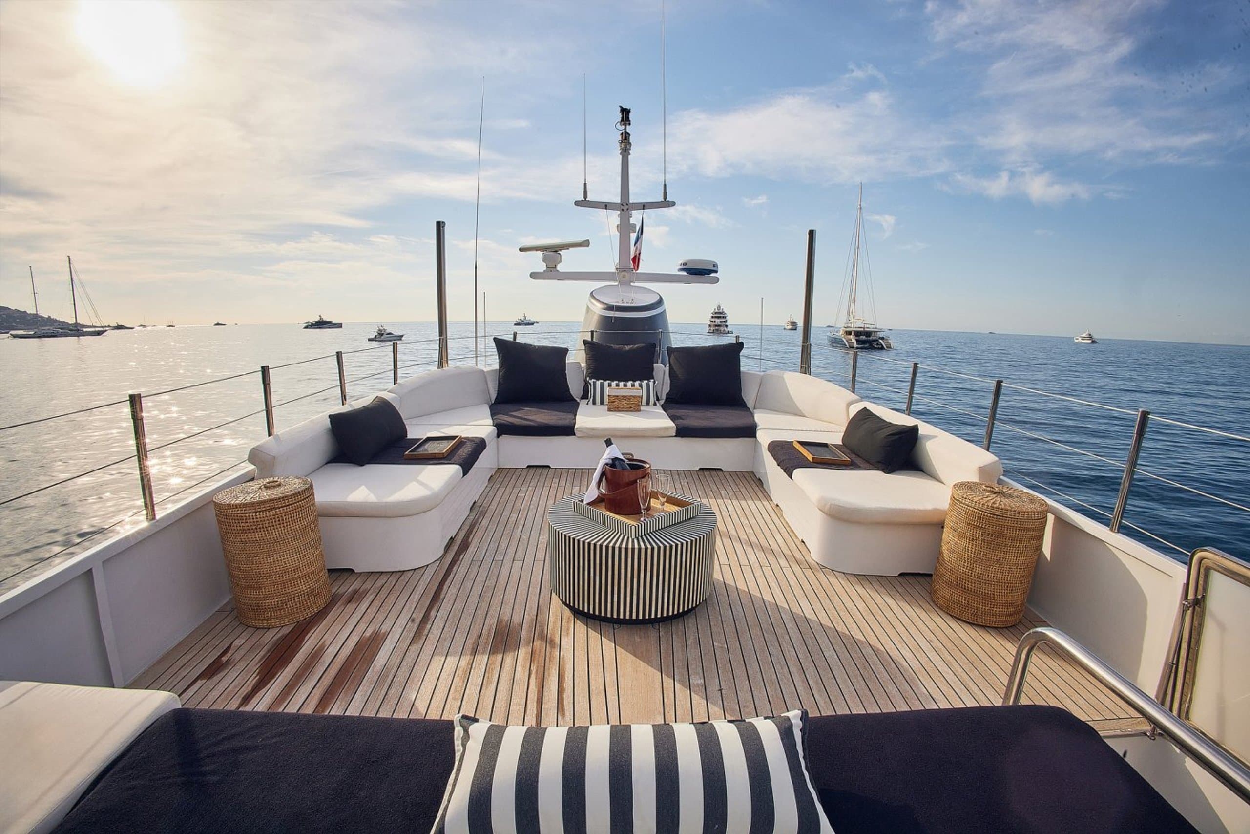 SOUNION II - upper deck lounge with white sofas, navy cushions and rattan side tables overlooking anchored yachts | Drivas Yachts
