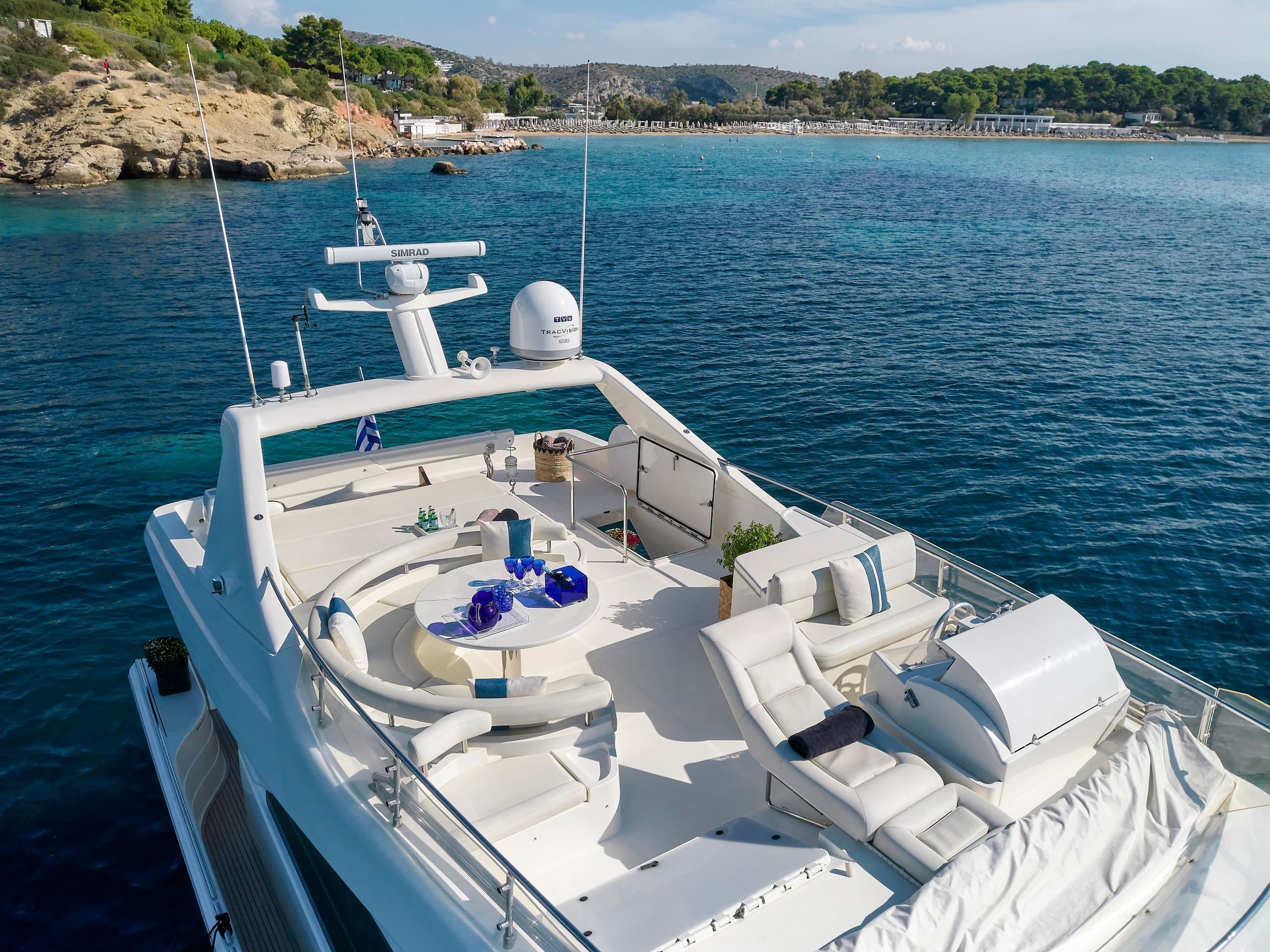 MIREN - flybridge with round alfresco dining table and white seating beneath the radar arch, coastline behind | Drivas Yachts