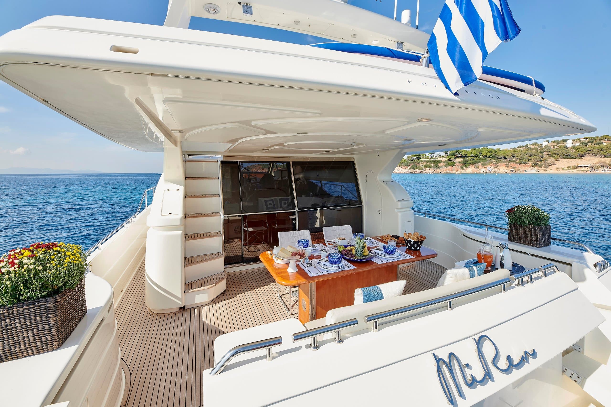 MIREN - shaded aft deck with alfresco dining table set on teak, Greek flag flying over calm water | Drivas Yachts