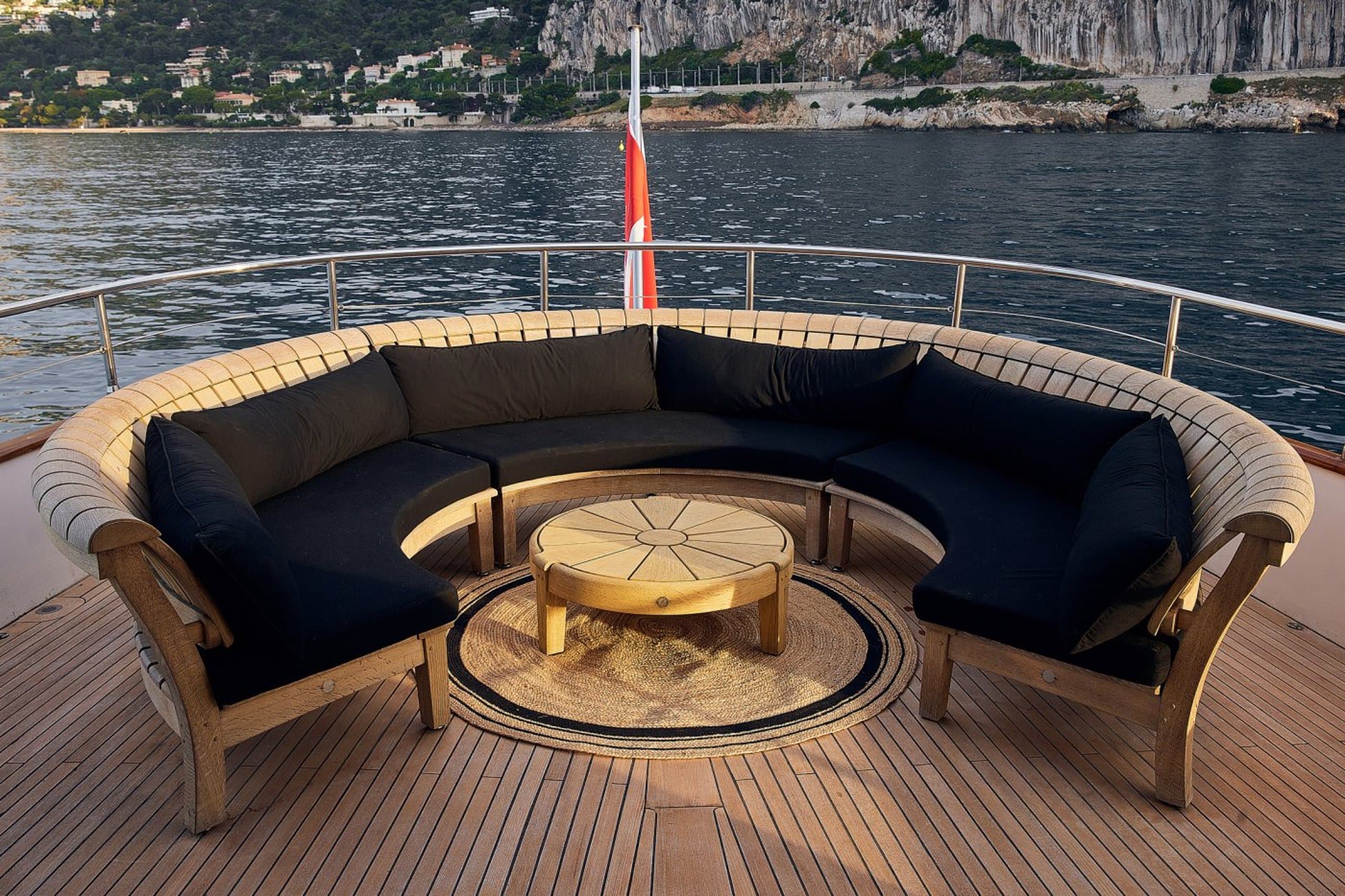 SOUNION II - curved teak aft-deck sofa with navy cushions and round table on the wooden deck | Drivas Yachts