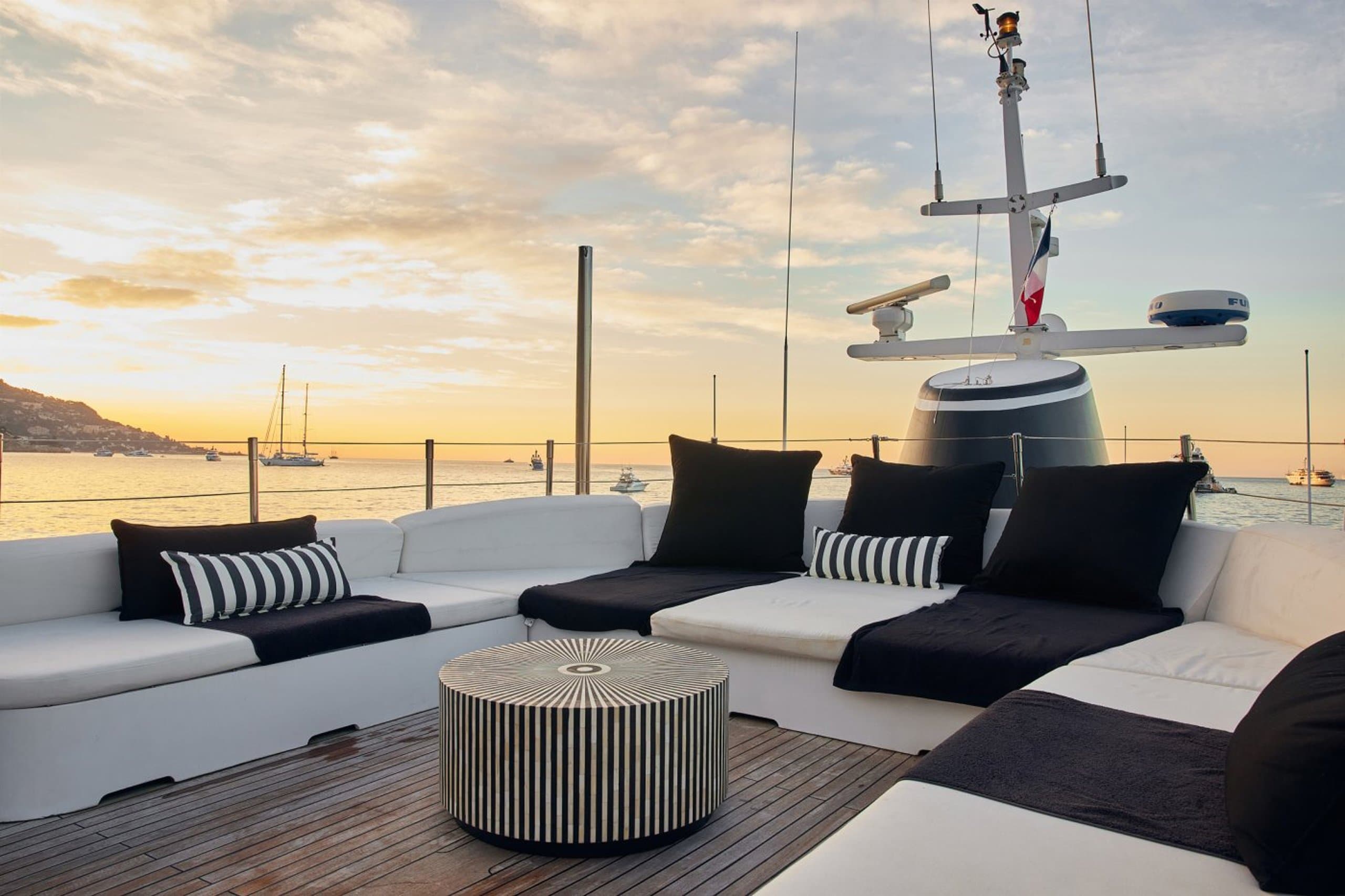 SOUNION II - deck lounge with white and navy cushioned seating at golden sunset | Drivas Yachts