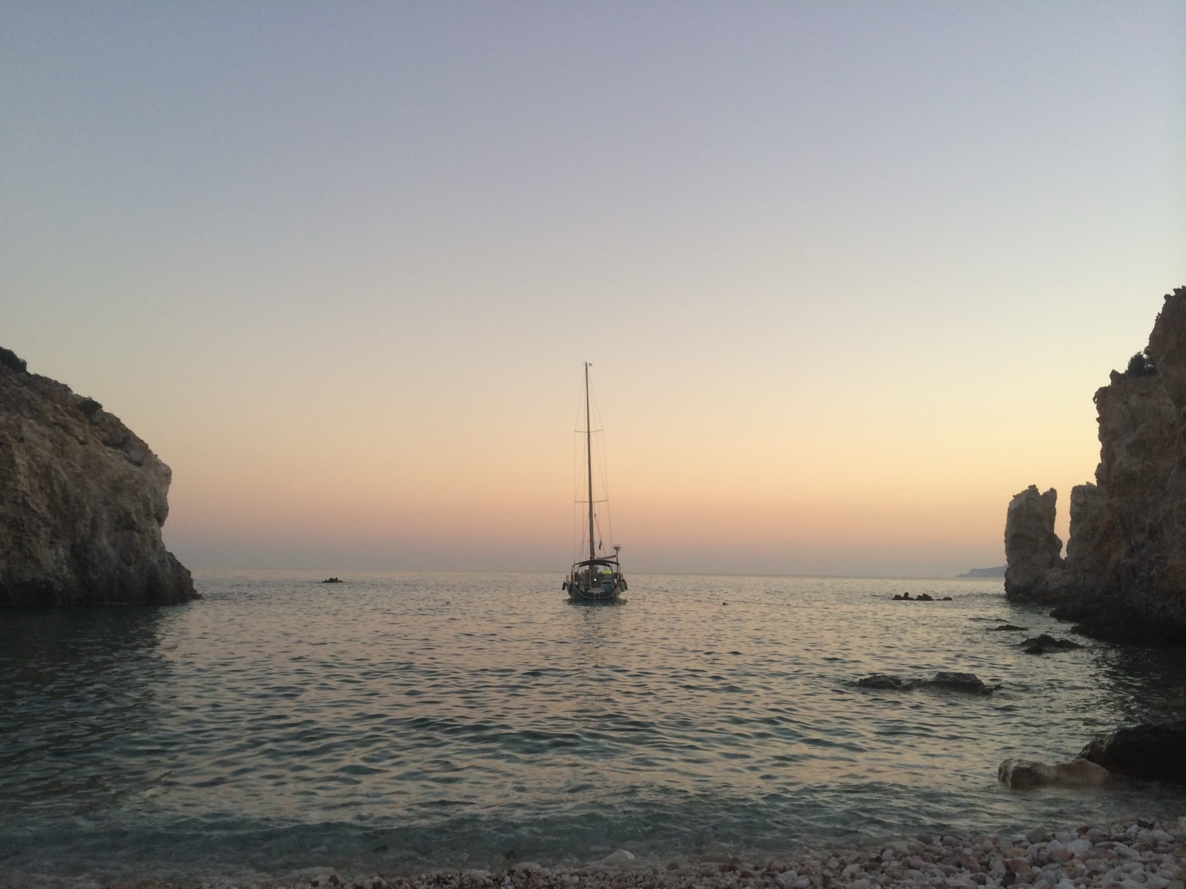 A sailing yacht at anchor between the rocks of Polyaigos at dusk