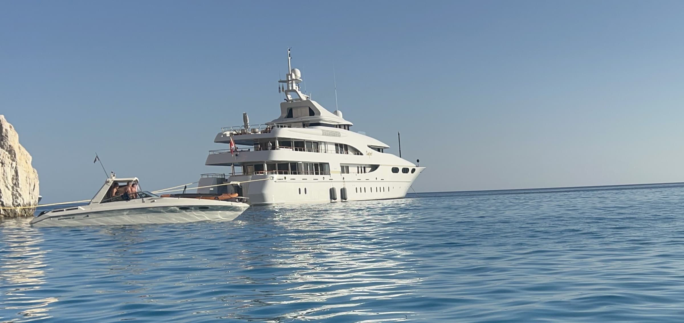 A charter yacht and its tender at anchor off the cliffs of Polyaigos