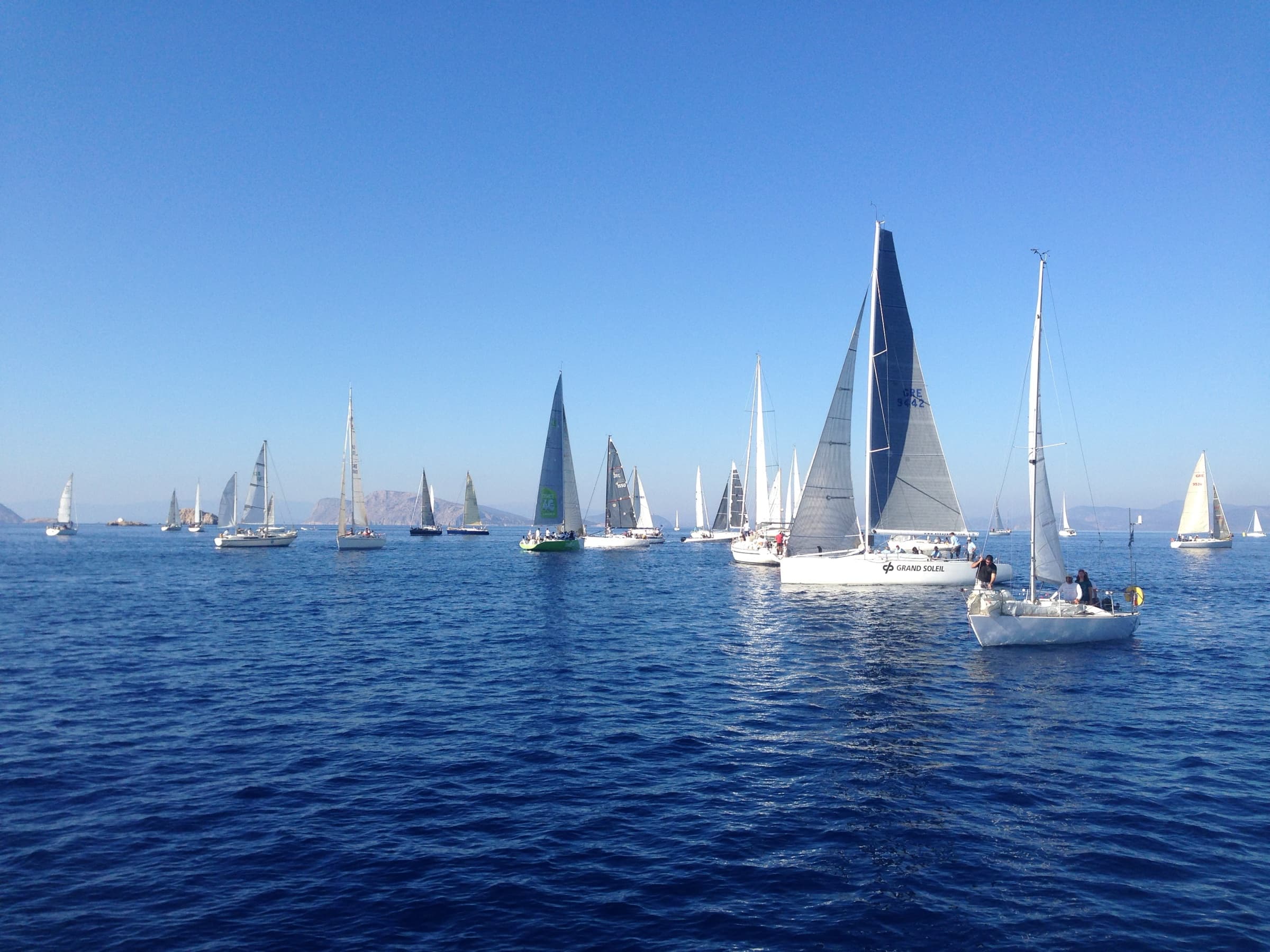 A fleet of sailing yachts at an offshore race start near Hydra
